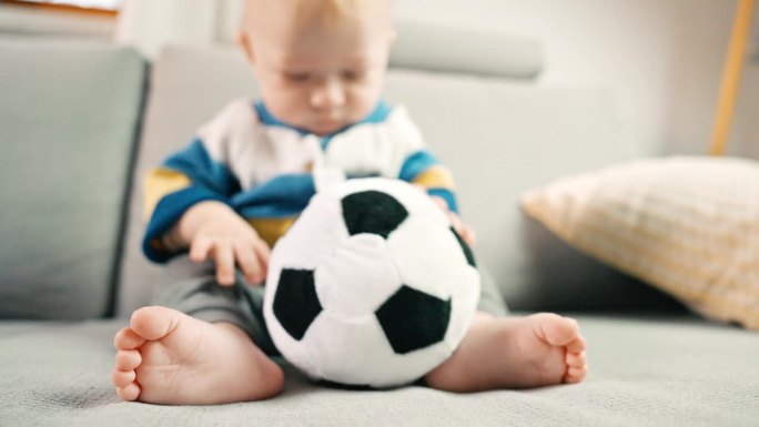 可爱的小男孩在沙发上玩柔软的足球玩具