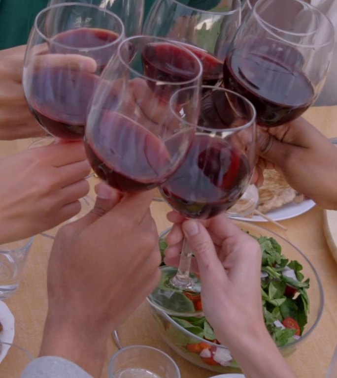 手在摆满食物的桌子上用红酒敬酒的特写。一群面目全非的朋友
