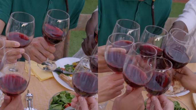 手在摆满食物的桌子上用红酒敬酒的特写。一群面目全非的朋友