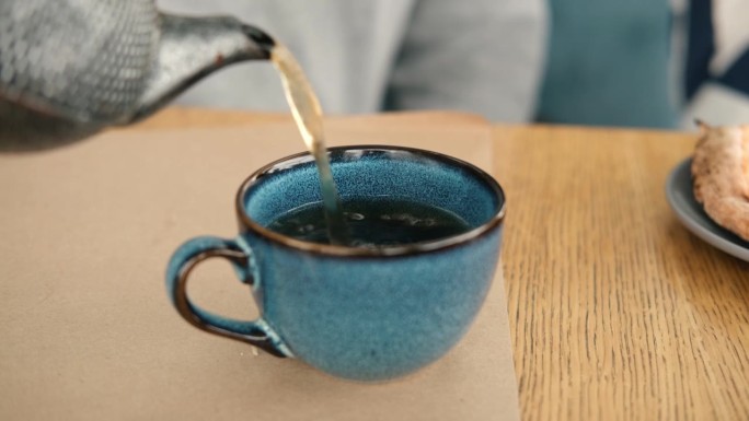 泡茶和上茶。在木制的咖啡桌上，用蓝色陶瓷杯倒绿茶的茶壶。清晨的两个陶器手工马克杯。时尚正宗瓷器套装。