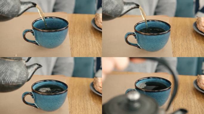 泡茶和上茶。在木制的咖啡桌上，用蓝色陶瓷杯倒绿茶的茶壶。清晨的两个陶器手工马克杯。时尚正宗瓷器套装。