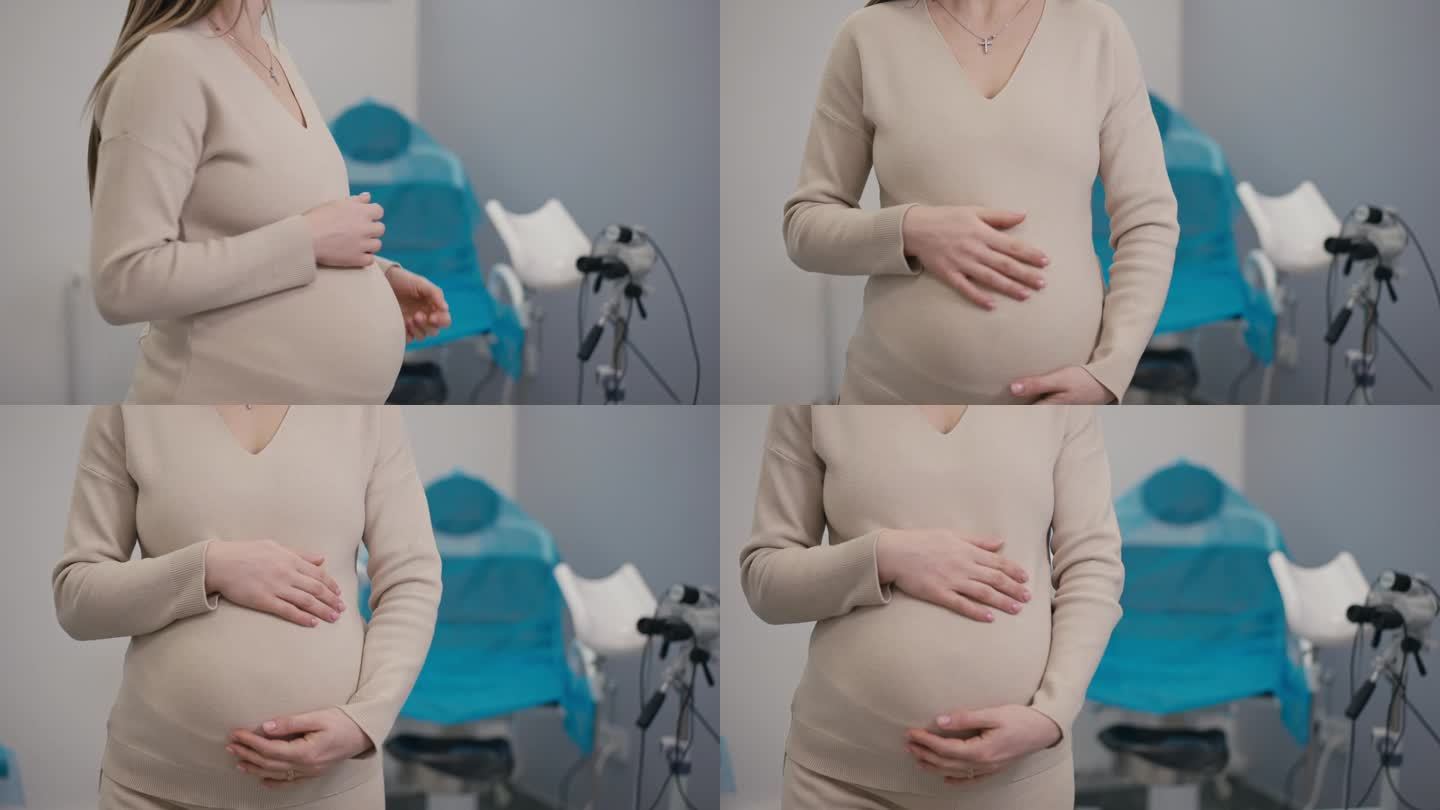 一名无法辨认的孕妇站在妇科椅旁，转向镜头，用手抱住自己的小肚子。