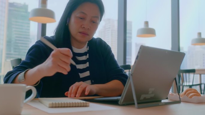 亚洲人在咖啡厅用笔记本电脑远程工作时，在数据表中写想法