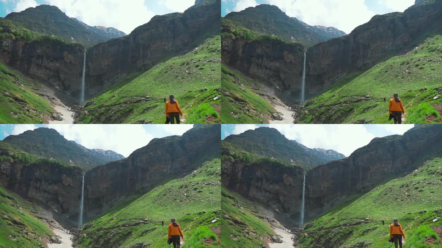 徒步旅行的少女徒步前往印度喜马偕尔邦拉胡尔的Sisu瀑布。山景与瀑布和绿色的草地在小径上。暑假期间去