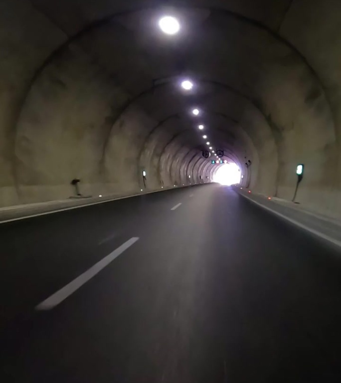 汽车驶出隧道，公路上一片漆黑。从汽车镜头显示隧道出口，强调汽车，隧道过渡。捕捉汽车，隧道出口进入高速