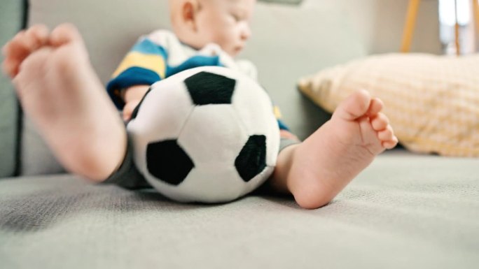 小男孩坐在家里的沙发上玩柔软的足球玩具