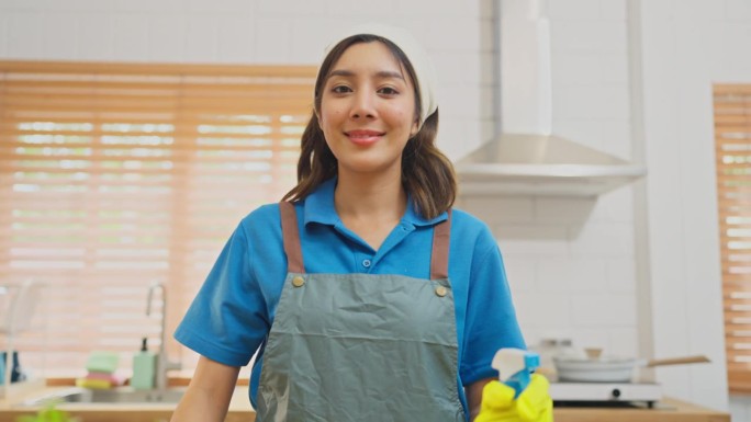 亚洲女管家或女女佣在顾客家的厨房里打扫桌子，然后微笑着看着镜头。