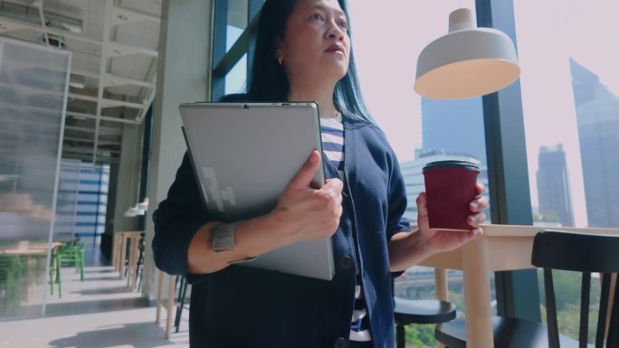 亚洲休闲女性拿着笔记本电脑和咖啡走进咖啡馆远程工作