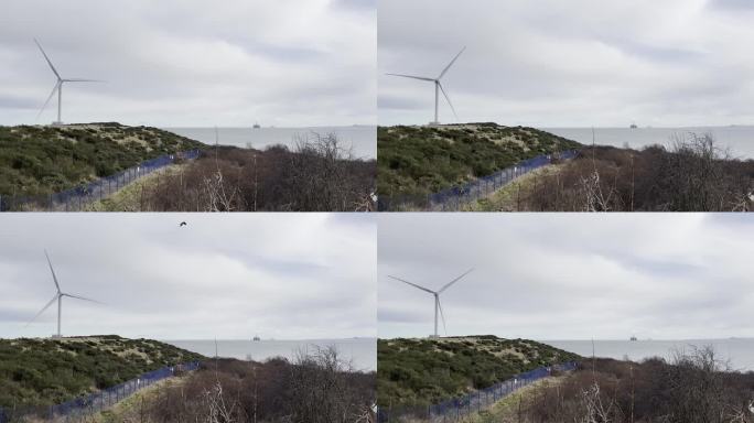 风力涡轮机在前景中快速旋转，而在远处可以看到北海的海上石油钻井平台