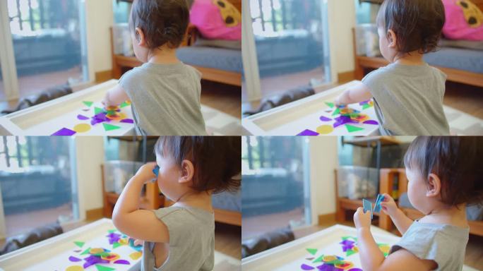 一个蹒跚学步的孩子在光桌上玩半透明的彩色形状，展示了一个明亮的、吸引人的活动，刺激感官和认知的发展