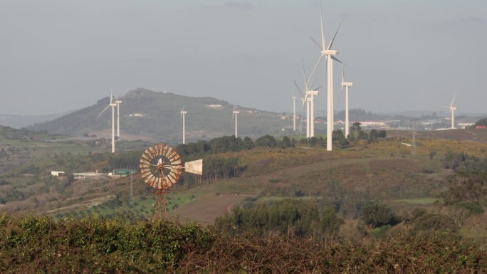风力涡轮机发电的画面，散布在丘陵地带，绿意盎然。