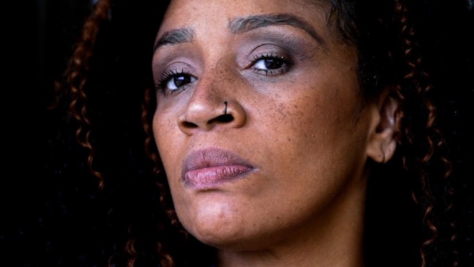 一个严肃的黑人中年妇女的特写脸，用紧张的目光盯着镜头，一种50年代美国黑人女性的不安的评判的表情