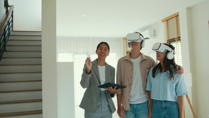 亚洲女房地产经纪人在新房子里用VR和平板电脑向租客解释和展示租或买。房东把房产卖给幸福夫妇客户。