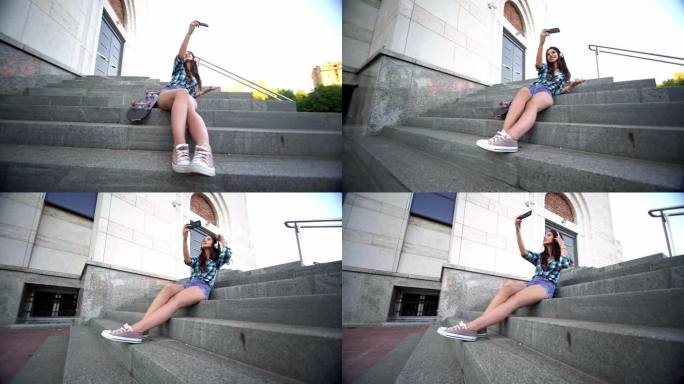 年轻的潮女手拿滑板坐在城市的台阶上自拍