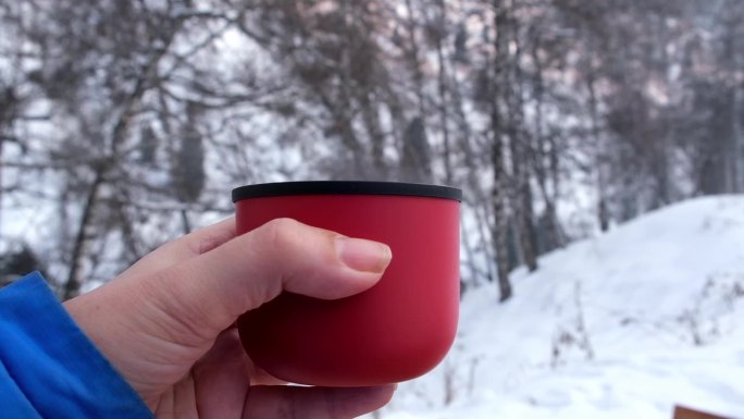 暖水瓶里的红色杯子，热气从热饮、茶或咖啡中冒出来，背景是冬天山里的白雪皑皑的森林