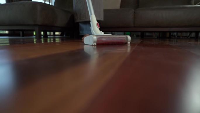 亚洲妇女在地板上用吸尘器清洁的特写镜头，家庭主妇在家里做家务，现代吸尘器在木地板上工作的特写镜头，家