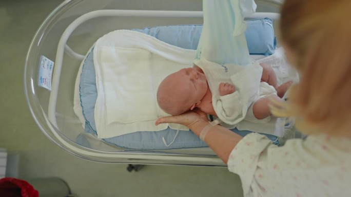 医管局母亲的护理:为躺在医院婴儿床上的婴儿穿紧身衣