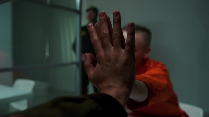 悲伤的女囚犯隔着玻璃与探访者握手