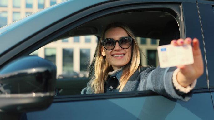 快乐的女人向车窗外展示她的新驾照