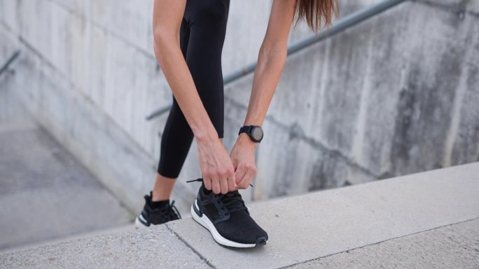 年轻的健身女性在运动鞋上系鞋带，准备跑步