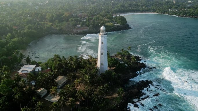 无人机灯塔在多岩石点在东德拉头，斯里兰卡。海浪冲击着被绿色植物包围的悬崖。历史灯塔巍然屹立，指引着水