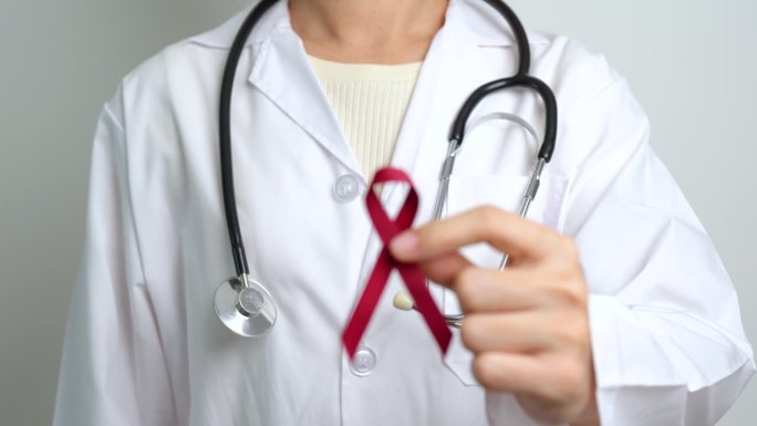 为3月多发性骨髓瘤癌症和12月世界艾滋病日宣传月佩戴酒红色丝带的医生。保健和世界癌症日概念