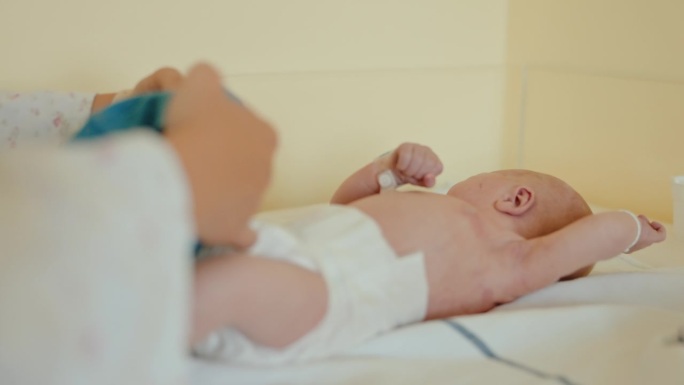 母亲的护理:给躺在医院婴儿床上的婴儿穿紧身衣