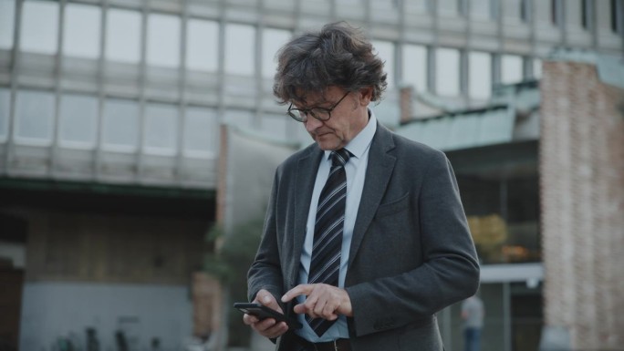 成熟男子在办公大楼使用智能手机的背景。商人在城市中使用智能手机