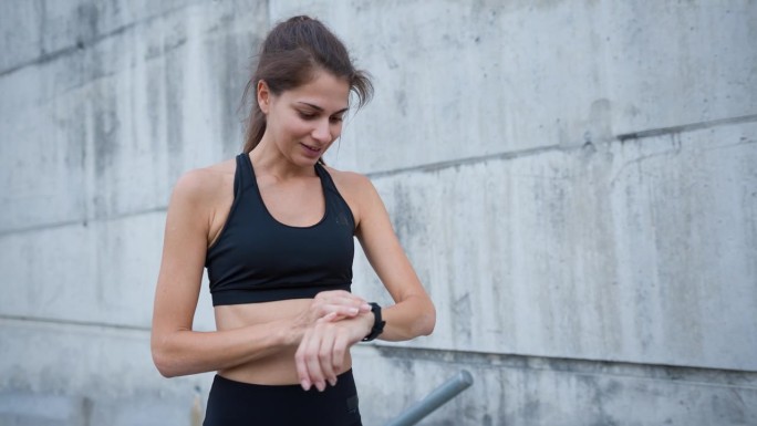 健康的女性跑步者在跑完城市楼梯后检查智能手表上的脉搏痕迹