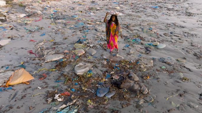 航拍缩小。在塞内加尔的达喀尔，一名卖鱼的黑人妇女头上顶着一个篮子，穿过鱼市海边可怕的塑料污染