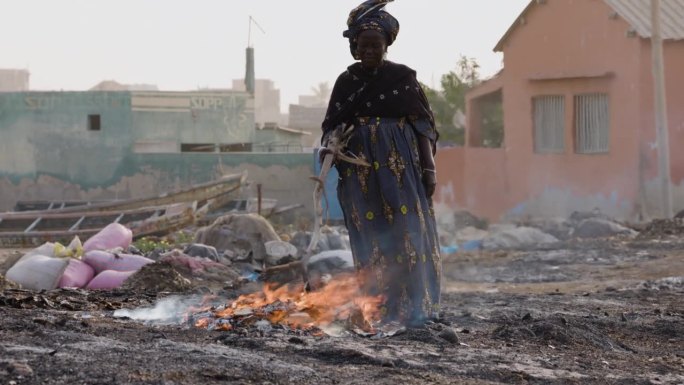 特写镜头。上了年纪的非洲黑人妇女在木片上熏小鱼。空气污染。塞内加尔达喀尔