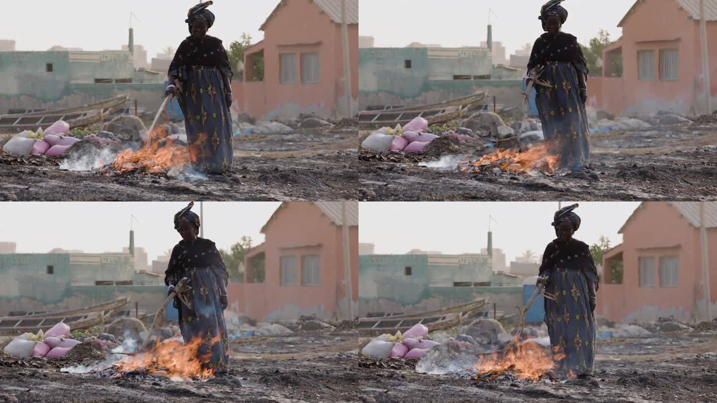 特写镜头。上了年纪的非洲黑人妇女在木片上熏小鱼。空气污染。塞内加尔达喀尔