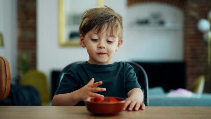 可爱的小男孩在家里的厨房柜台上吃草莓，俯瞰客厅的背景。金发白人小孩吃零食的画像