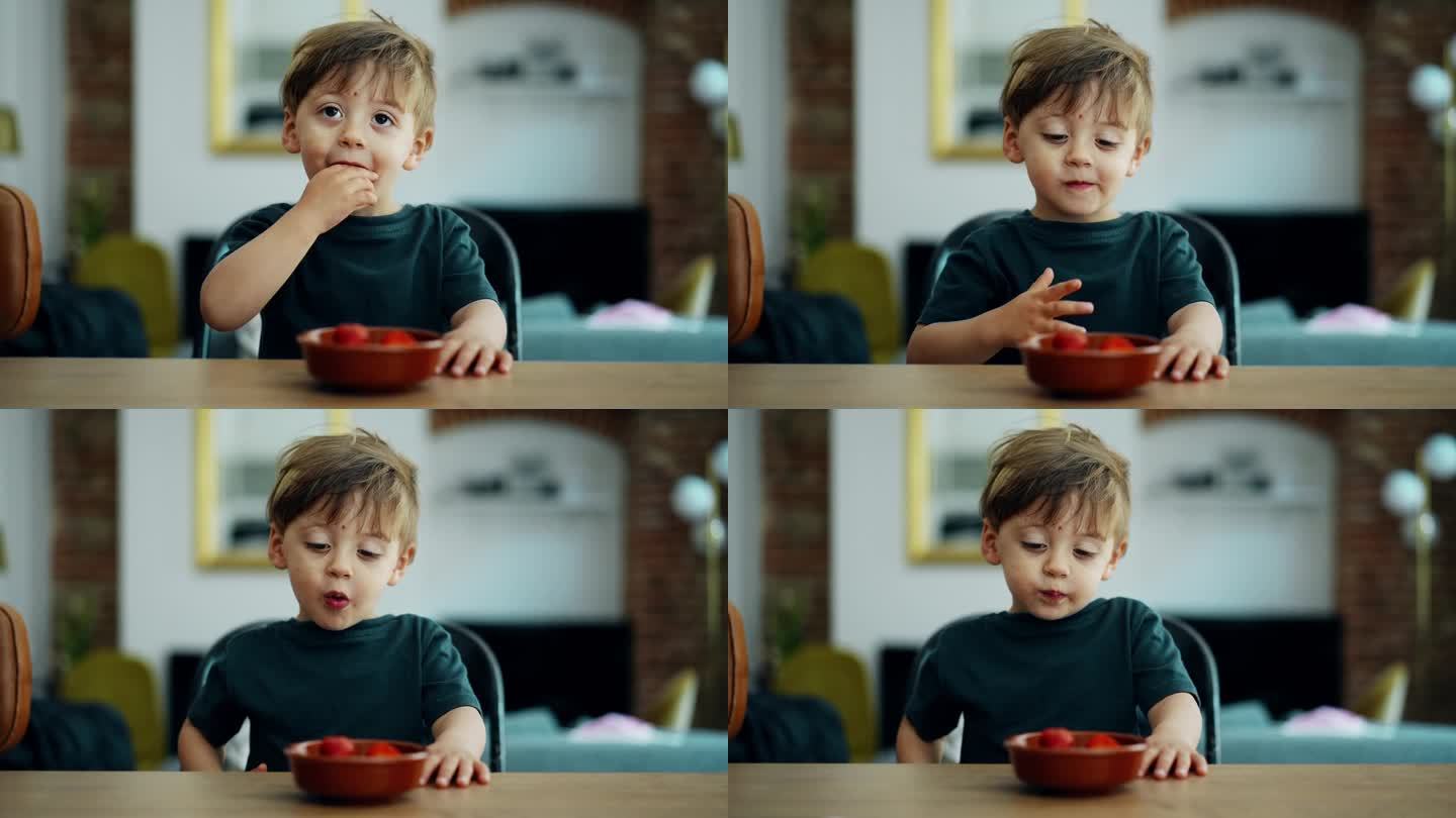 可爱的小男孩在家里的厨房柜台上吃草莓，俯瞰客厅的背景。金发白人小孩吃零食的画像