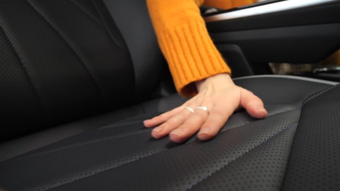 汽车内部装饰的纹理。汽车座椅的设计。一只手摸着汽车座椅。一只手抚摸着一辆高档汽车的内部。