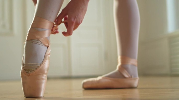 芭蕾舞女演员在舞蹈课上把脚尖鞋穿在腿上。古典芭蕾舞女演员在舞蹈工作室。芭蕾舞女演员穿上系着古典尖头鞋