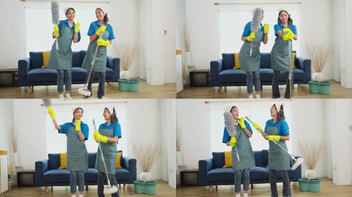 两个亚洲女管家或女佣站在一起，拿着清洁房子的工具，快乐地跳舞。