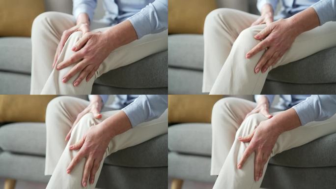坐在家里客厅沙发上的资深女性用手按摩膝盖腿部肌肉。