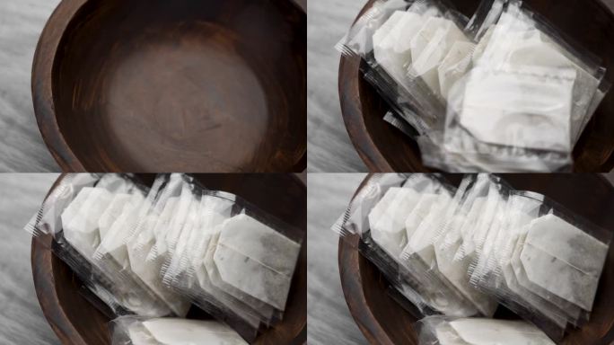 一堆凉茶包以慢镜头落入一个木碗(特写)。健康芳香饮料成分