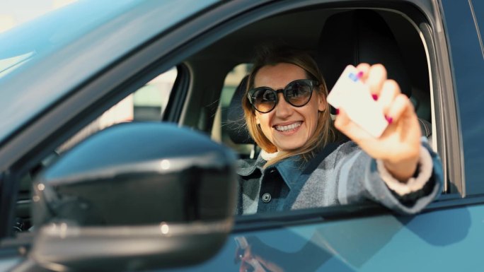 快乐的女人向车窗外展示她的新驾照，然后开车走了