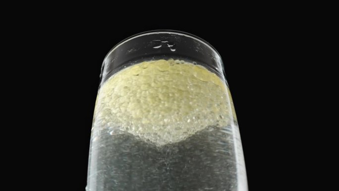 一个黑色背景的玻璃杯，里面有油泡在水里旋转。玻璃杯里有气泡。