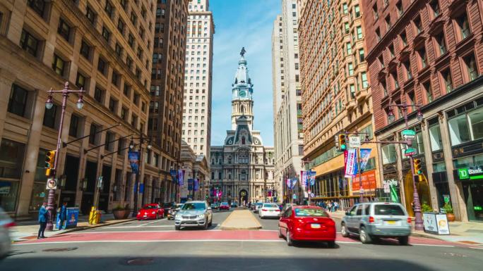 美国宾夕法尼亚州费城的地标性历史建筑市政厅，交通车辆和拥挤的行人穿过城市街道