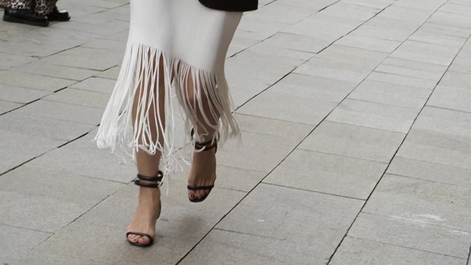 时尚女性的双腿，在户外的城市街道上，穿着带流苏的夏季连衣裙和高跟鞋。