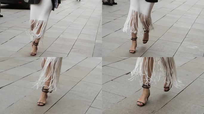 时尚女性的双腿，在户外的城市街道上，穿着带流苏的夏季连衣裙和高跟鞋。