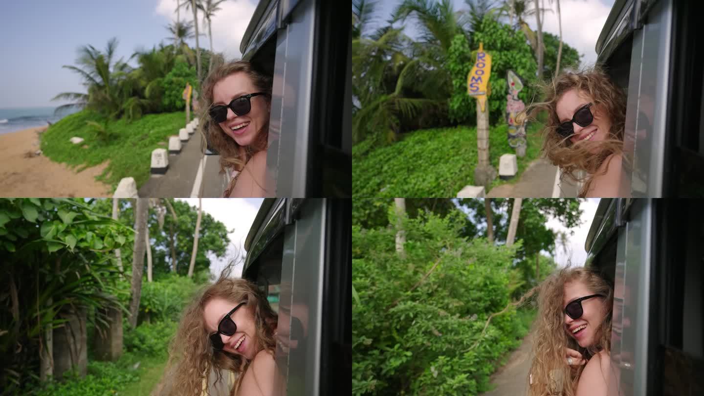 一个快乐的女孩，她有一头飘逸的卷发，在穿过热带森林时看着车窗外。年轻女子微笑着，从行驶中的汽车窗口探