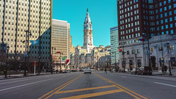 美国宾夕法尼亚州费城的地标性历史建筑市政厅，交通车辆和拥挤的行人穿过城市街道