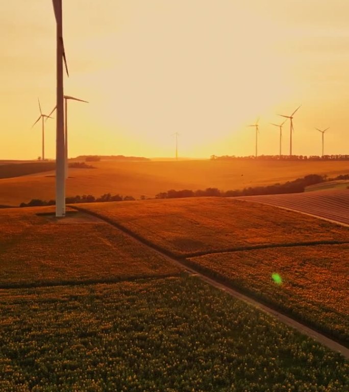 空中乡村复兴:日落无人机镜头捕捉风力涡轮机，田地，和一辆汽车走向清洁能源