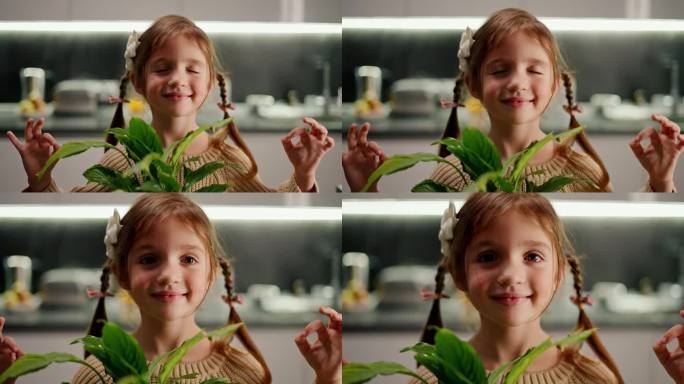 一个快乐平静的棕色头发的小女孩的特写，她梳着辫子，坐在莲座上，晚上在现代厨房里与室内植物一起练习禅宗