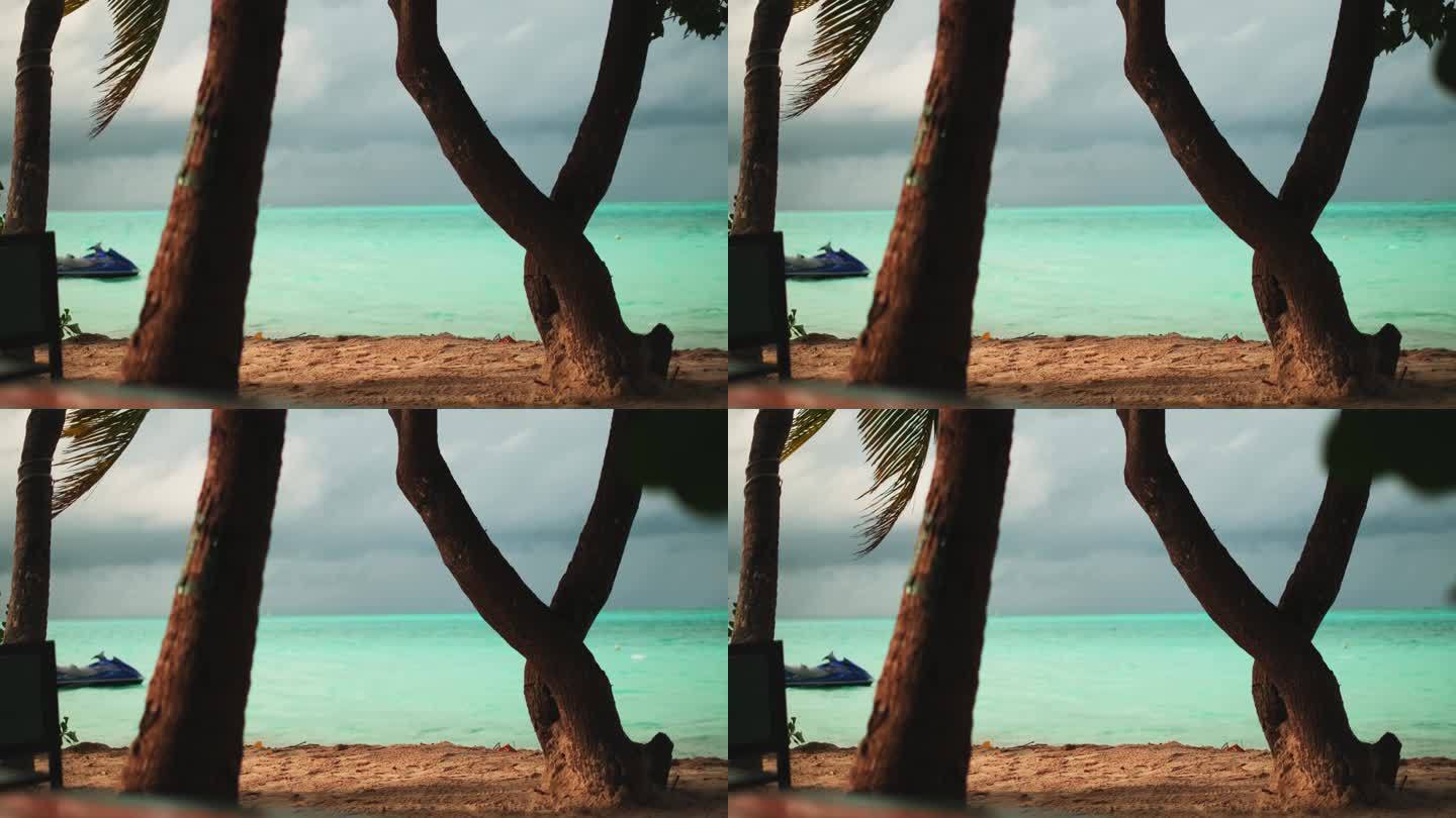沙滩上的热带棕榈树。在海湾里，一艘水上摩托艇在波浪上滑行，背景是多云的日落天空。马尔代夫。