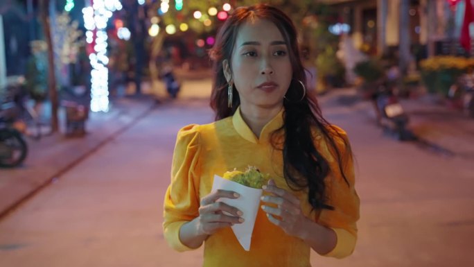 越南会安，身着传统服装的年轻越南女子晚上吃着当地披萨的慢动作跟随镜头
